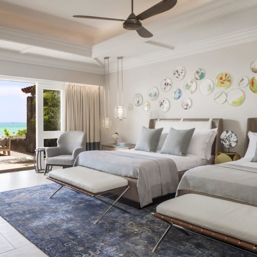 Luxuriöses Twin-Schlafzimmer mit Meerblick, in neutralen Tönen gestaltet, mit Schiebetüren zum Balkon mit Sitzgelegenheiten und Meerblick.