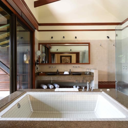 Luxury rainforest bathroom with a large jacuzzi tub, wooden accents, and glass walls overlooking lush greenery.