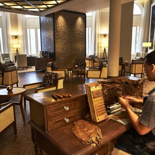 Ein Mann sitzt an einem Tisch in einem luxuriösen Lounge, arbeitet an der Herstellung von Zigarren mit Tabakblättern und Werkzeugen.