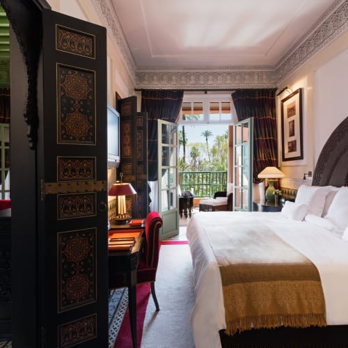 Luxuriöse Hotellandsuite mit eleganter Einrichtung, großem Bett mit weißen Bettwäsche und Balkon mit Blick auf Grünanlagen.