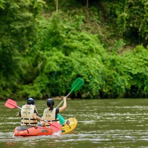 Drei Personen in einem Kajak auf einem Fluss mit üppigen grünen Bäumen im Hintergrund und paddeln zusammen.