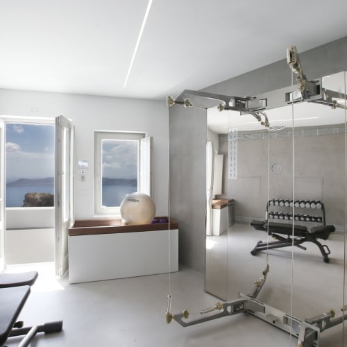 Fitnessraum mit großen Fenstern, die den Meerblick zeigen, Spiegel und Trainingsgeräte in einem modernen, hellen Inneren.