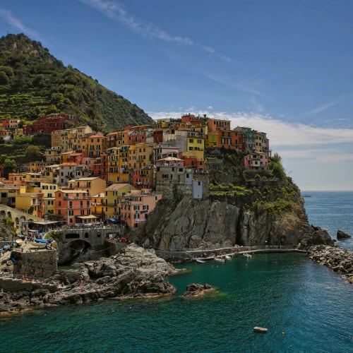 Bunte Häuser, die steil an Klippen liegen und auf das türkisfarbene Meer in einem malerischen Küstendorf in Ligurien, Italien, blicken, bei klarem Himmel.