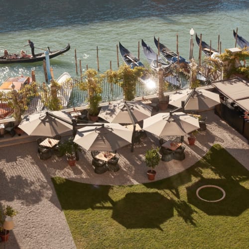Eine malerische Uferterrasse mit Sonnenschirmen, Tischen und Gondeln am Wasser in Venedig.