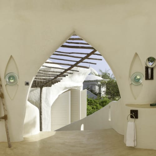 Bathroom in a Kilindi room with two white basins, bamboo shelves, and a scenic view of trees and sky through arched windows.