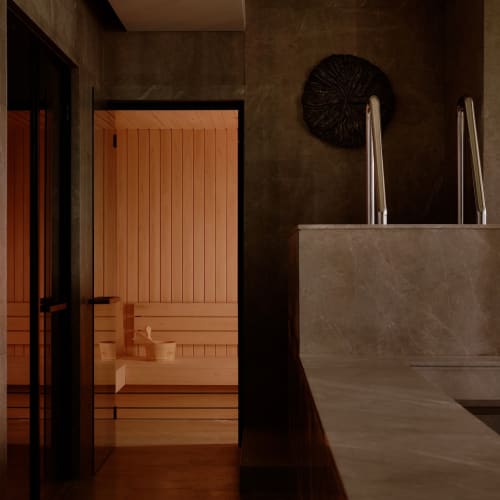 A modern sauna room with wooden benches and a partial view of a swimming pool on the right.