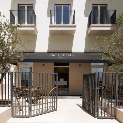 Der Eingang des The Lumiares Hotels & Spa mit einem schwarzen Vordach und einem Außenbereich mit Sitzgelegenheiten, eingeschlossen durch ein Metalltor, flankiert von zwei Olivenbäumen.