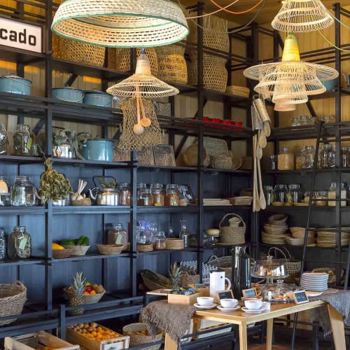 Interior of a shop with shelves filled with glass jars, dishes, and kitchenware, decorated with woven lampshades.