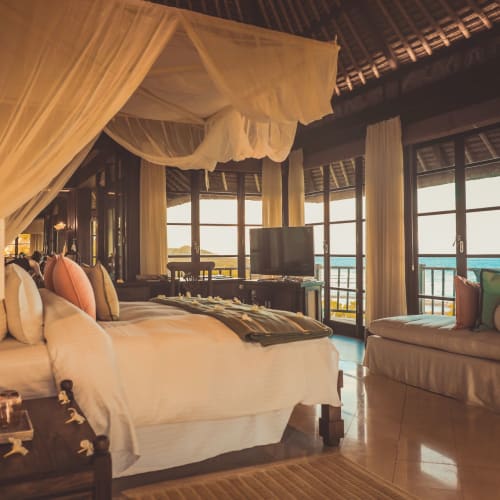 Luxurious bedroom with canopy bed, large windows with ocean view, and elegant furnishings in a villa on Fregate Island, Seychelles.