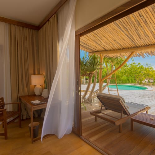 Ein Villinnenraum öffnet sich zu einer Terrasse mit Liegen, einem Hot Tub und üppigem Grün.
