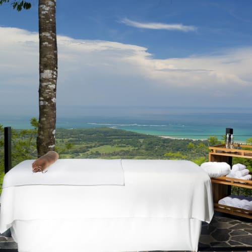 A massage table set up inside with a view of lush green landscape and the ocean in the distance.