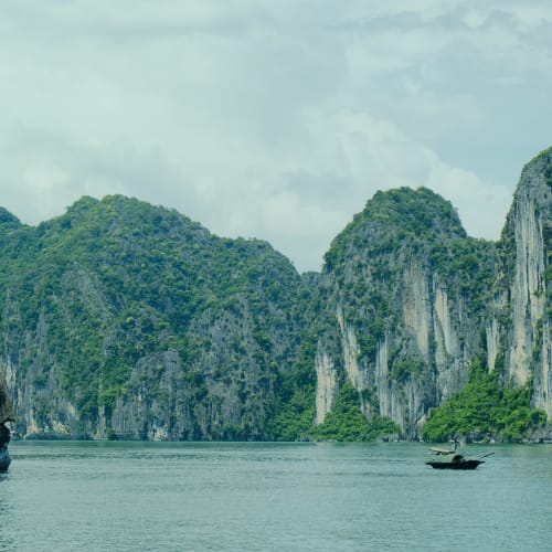 Eine malerische Ansicht von Halongbucht in Vietnam mit Kalkstein-Karsts und einem kleinen Boot auf dem Wasser.