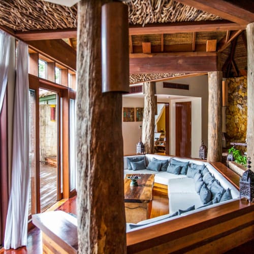 Heller Wohnraum mit einer gebogenen Couch, großen Fenstern und Holzelementen in einer tropischen Inselvilla.