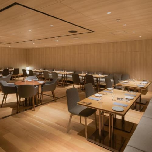 A modern restaurant with wooden walls and ceiling, featuring neatly arranged tables and chairs with place settings.