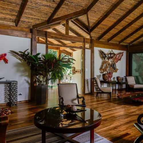 Elegant living area inside a Costa Rican lodge with wooden decor, large plants, and colorful wall art.