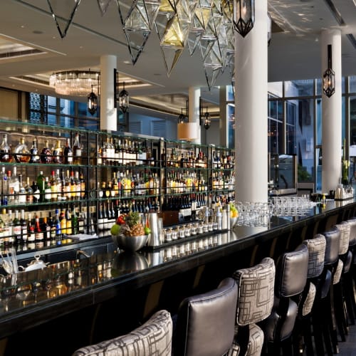 Elegante Hotelbar mit dunkem Marmor-Theke, Reihe von Spirituosenflaschen und modernen hängenden Leuchten in einem luxuriösen Ambiente.