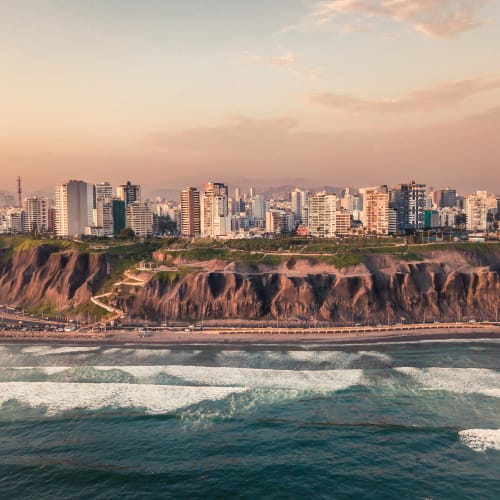 Sunset over a coastal city with high-rise buildings and cliffs along the shoreline.