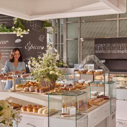 Eleganter Kuchenladen im Mandarin Oriental Tokyo mit Glasvitrinen voller verschiedenster Gebäck und Kuchen, und zwei Frauen im Gespräch.