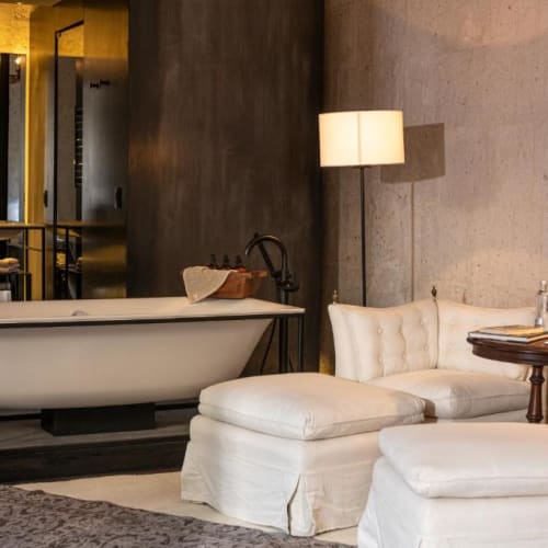 A luxurious bathroom with a freestanding bathtub and a cozy seating area with white upholstered furniture.