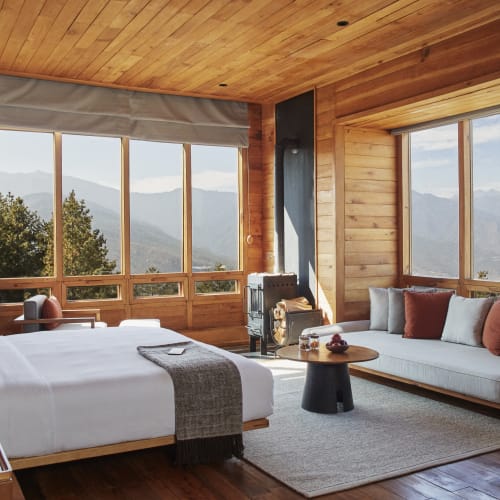 Ein gemütliches Schlafzimmer aus Holz mit großen Fenstern, die Bergblick bieten, einem Bett und einem Sitzbereich mit Sofa und kleinem Tisch.