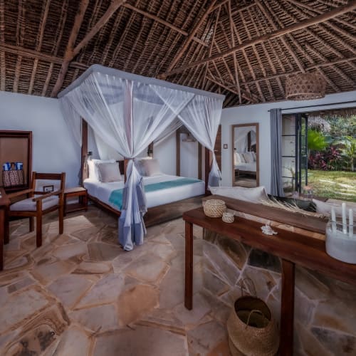 A spacious room with a large canopy bed, wooden furniture, and a sliding glass door leading to a garden view.