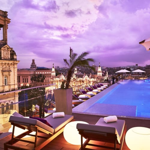Nächtlicher Blick auf einen luxuriösen Poolbereich auf einem Dach in Habana mit Stadtbild und historischen Gebäuden im Hintergrund.