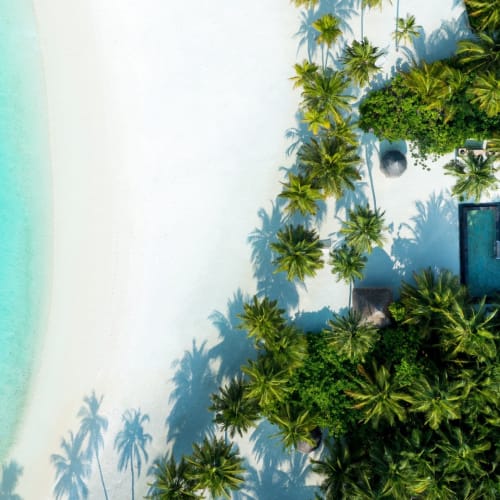 Aerial view of a luxurious resort with sandy beach, clear turquoise water, and lush greenery on the Maldives.