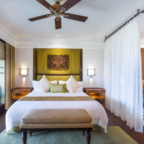 Luxus Suite in einem tropischen Resort mit einem geräumigen Schlafzimmer, elegant dekoriert, mit privatem Balkon und Sitzgelegenheit im Freien.