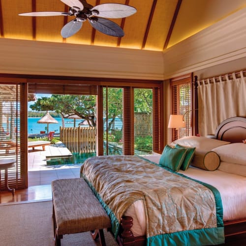 Ein luxuriöses Hotelzimmer mit einem großen Bett, Nachttischen und Blick auf den Pool und den Ozean durch große Glastüren.