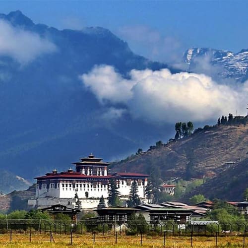 Landschaftlicher Blick auf das Gangtey-Tal in Bhutan mit traditionellen Gebäuden, umgeben von grünen Hügeln und nebligen Bergen im Hintergrund.
