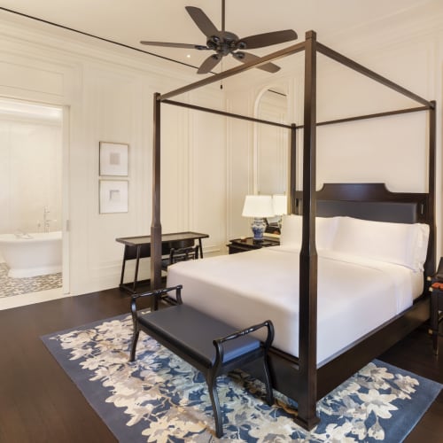 Elegant Schlafzimmer mit einem Himmelbett, dunklem Holzmobiliar und Blick in ein Badezimmer in einer luxuriösen Hotellsuite.