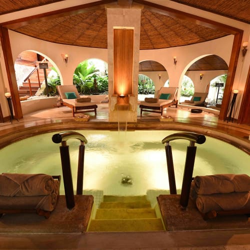 Luxury wellness pool in a tropical spa with lounge chairs and arches overlooking lush greenery.