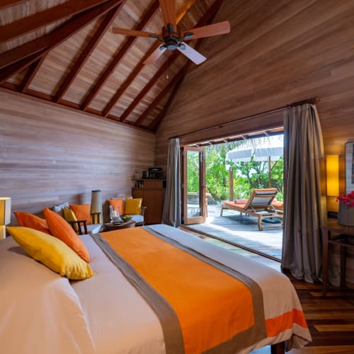 Innenraum einer gemütlichen Strandvilla mit großem Bett, bunten Kissen und Blick auf die Terrasse durch Glasschießen.