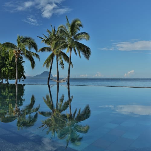 Infinity-Pool im Maradiva Villas Resort & Spa, der Palmen spiegelt, mit Ozean und Insel im Hintergrund unter einem teilweise bewölkten blauen Himmel.