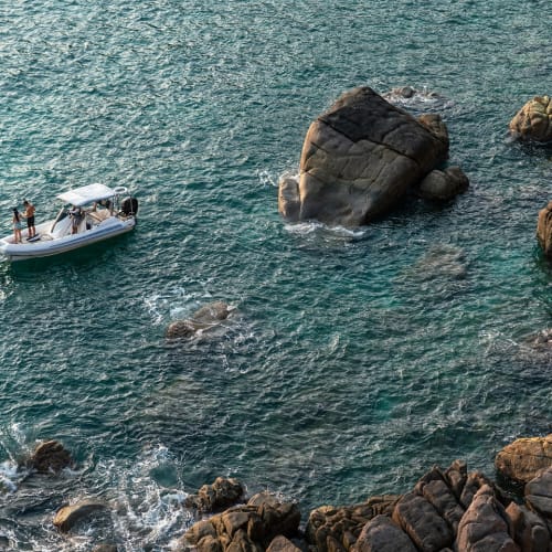 Ein Boot mit zwei Personen an Bord treibt in der Nähe von felsiger Küste im Wasser.