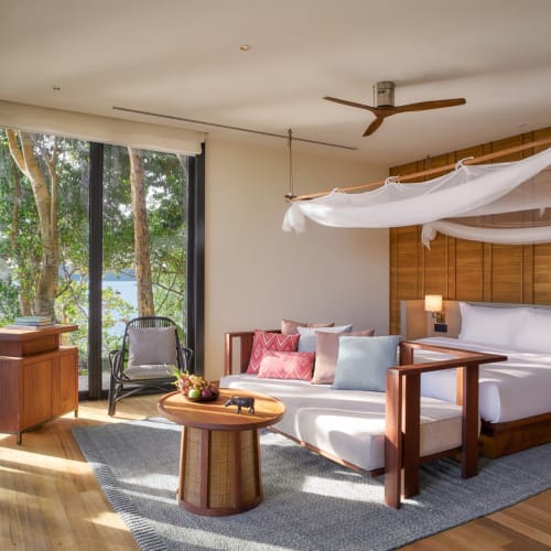 Schlafzimmer in der Ocean Pool Villa auf der Six Senses Krabey Island mit Holzmöbeln, großem Bett und einer Moskitonetz über dem Bett.