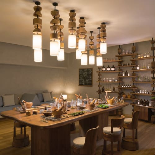 Ein gemütliches Esszimmer mit einem großen Holztisch, der für eine Mahlzeit gedeckt ist, umgeben von Stühlen, und dekoriert mit warmen hängenden Lichtern und Holzregalen, die mit Gläsern und Flaschen gefüllt sind.