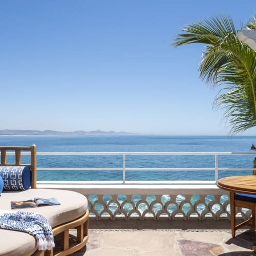 Eine luxuriöse Meeresblick-Terrasse mit Holzmöbeln, bunten Kissen und klarem blauen Himmel über dem Meer.