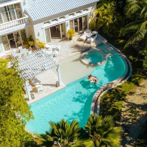 Eine private Villa mit einem geschwungenen Swimmingpool, Jacuzzi und Sitzbereich im Freien, umgeben von üppigem Grün bei Eden Roc Cap Cana.