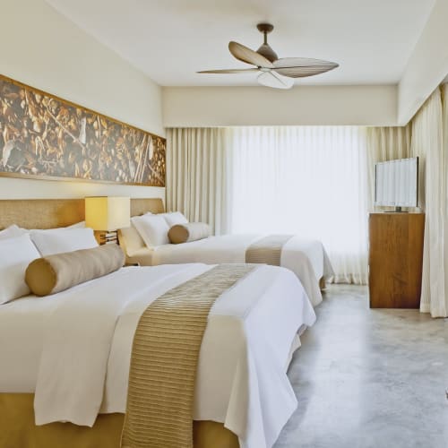 Interior of the El Mangroove Nesto Suite in Costa Rica with two large beds, a ceiling fan, and a view of the balcony.