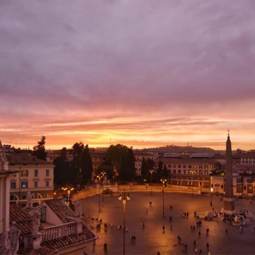 Sonnenuntergang über einem Platz in Rom mit historischen Gebäuden und Menschenmenge.