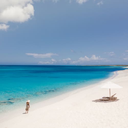 Eine Person spaziert an einem unberührten weißen Sandstrand mit klarem türkisfarbenem Wasser und blauem Himmel darüber.