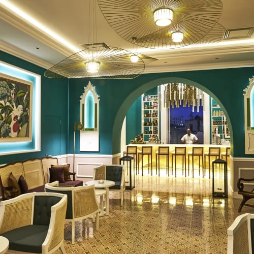 Elegant eingerichteter Aufenthaltsraum mit blauen Wänden, klassischer Einrichtung und Bar im Hintergrund, beleuchtet von modernen Deckenleuchten.