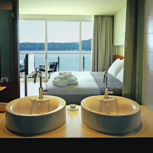 Luxuriöses Hotelzimmer mit zwei runden Waschbecken und Blick auf einen See oder das Meer durch große Fenster.
