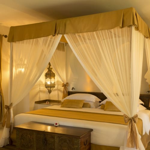 Luxuriöses Schlafzimmer mit einem Himmelbett, das mit transparenten Vorhängen in einem Resort in Sansibar drapiert ist.