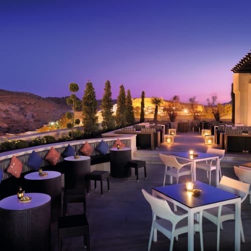 Eine stilvolle Dachterrasse im Moevenpick Resort Petra bei Abend, mit modernen Tischen und Stühlen, Kerzen und malerischem Bergblick.