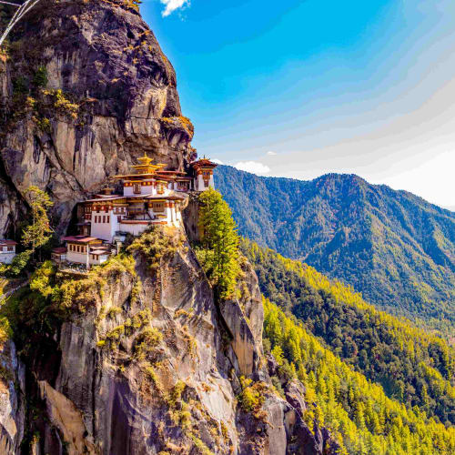 Panoramische Aussicht auf die Tiger's Nest Kloster, das an eine Klippe in Bhutan klebt, mit Bergen im Hintergrund.