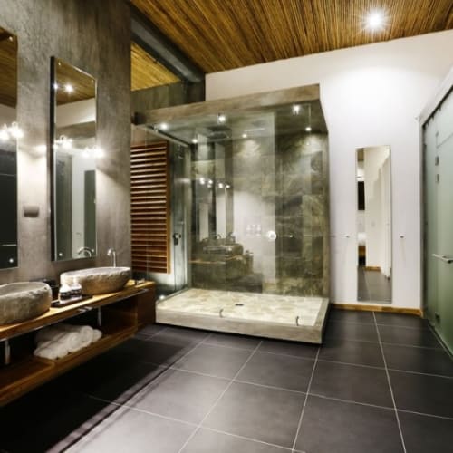Luxurious bathroom in a modern boutique hotel featuring stone sinks, mirrors, and a walk-in shower with glass walls.
