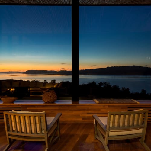 Interior view of a lounge with large windows overlooking a serene lake and sunset in Chile.