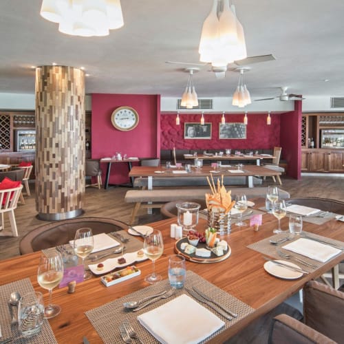 Geräumiges modernes Restaurant mit Holztischen und Stühlen, eingedeckt mit Tellern, Gläsern und Besteck, mit einer Holzsäule und Weingestellen im Hintergrund.